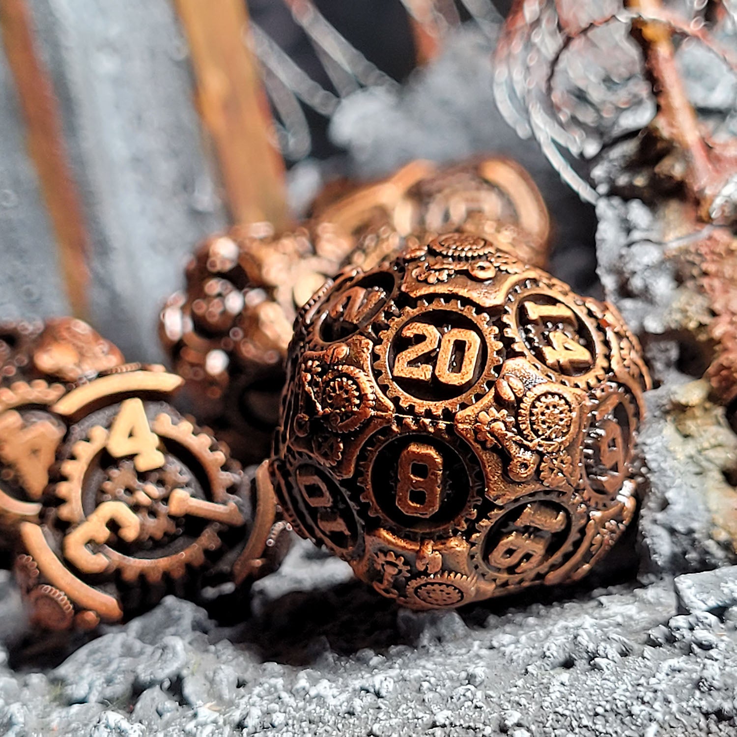 This is an environmental image of the Forged Gaming Chronomica Mechanicum Gold Metal RPG Dice Set. This photo was taken using pieces of razor wire wargaming terrain as a background.