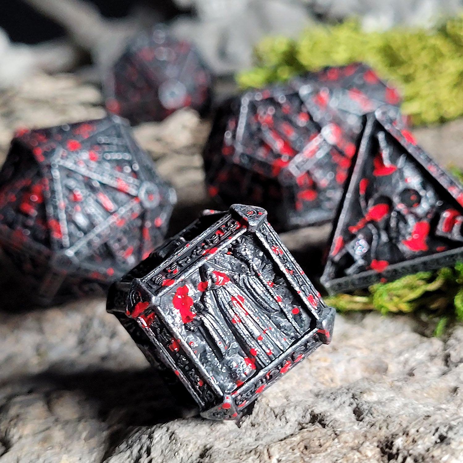 This is an environmental image of the Forged Gaming Cryptic Reliquary Silver Blood Metal RPG Dice Set. The photo was taken against a background of stone wargaming terrain.