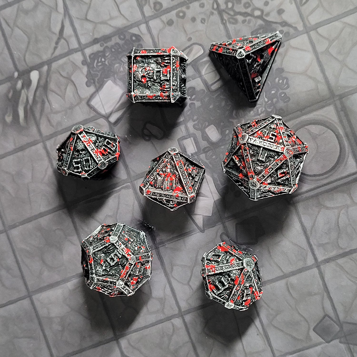 This is an environmental image of the Forged Gaming Cryptic Reliquary Silver Blood Metal RPG Dice Set. The photo was taken against the background of the Dungeon Floor Encounter Map.