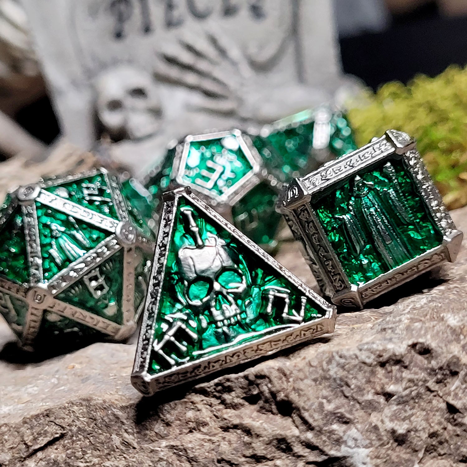 This is an environmental image of the Forged Gaming Cryptic Reliquary Silver Green Metal RPG Dice Set. The photo was taken against the backdrop of a piece of stone wargaming terrain.