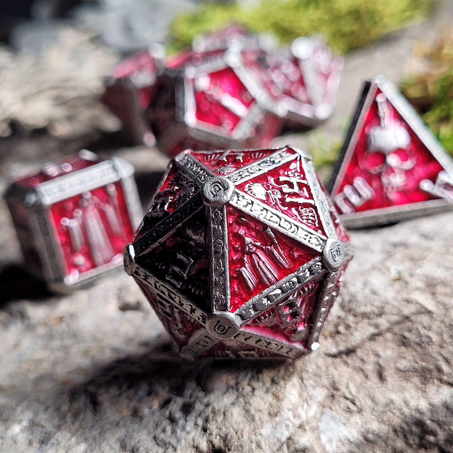 This is an environmental image of the Forged Gaming Cryptic Reliquary Silver Red Metal RPG Dice Set. The photo was taken against the backdrop of a piece of stone wargaming terrain.