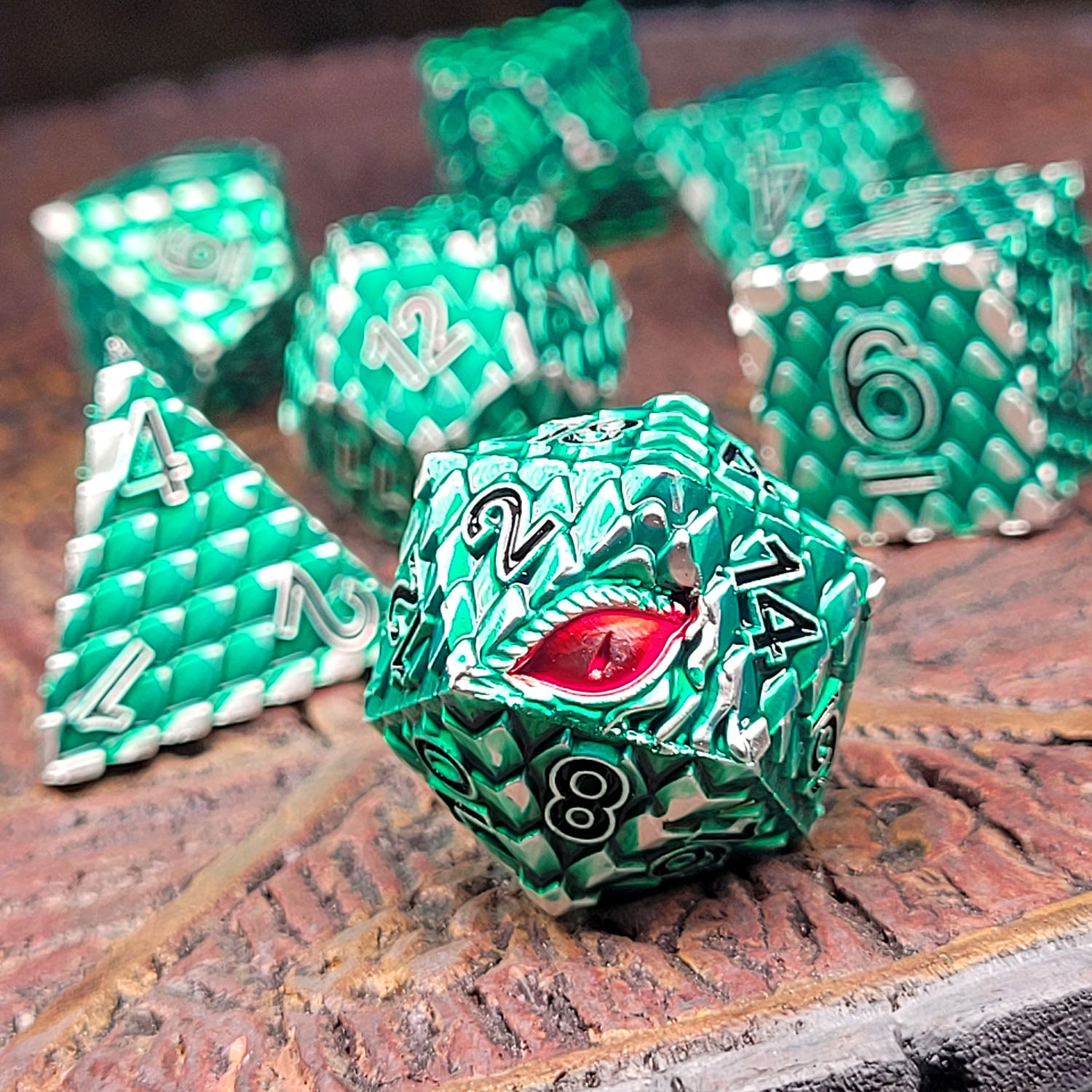 This is an environmental image of the Forged Gaming Dragon's Gaze Silver Green metal RPG dice set. The photo was taken using a piece of wargaming terrain as a background.