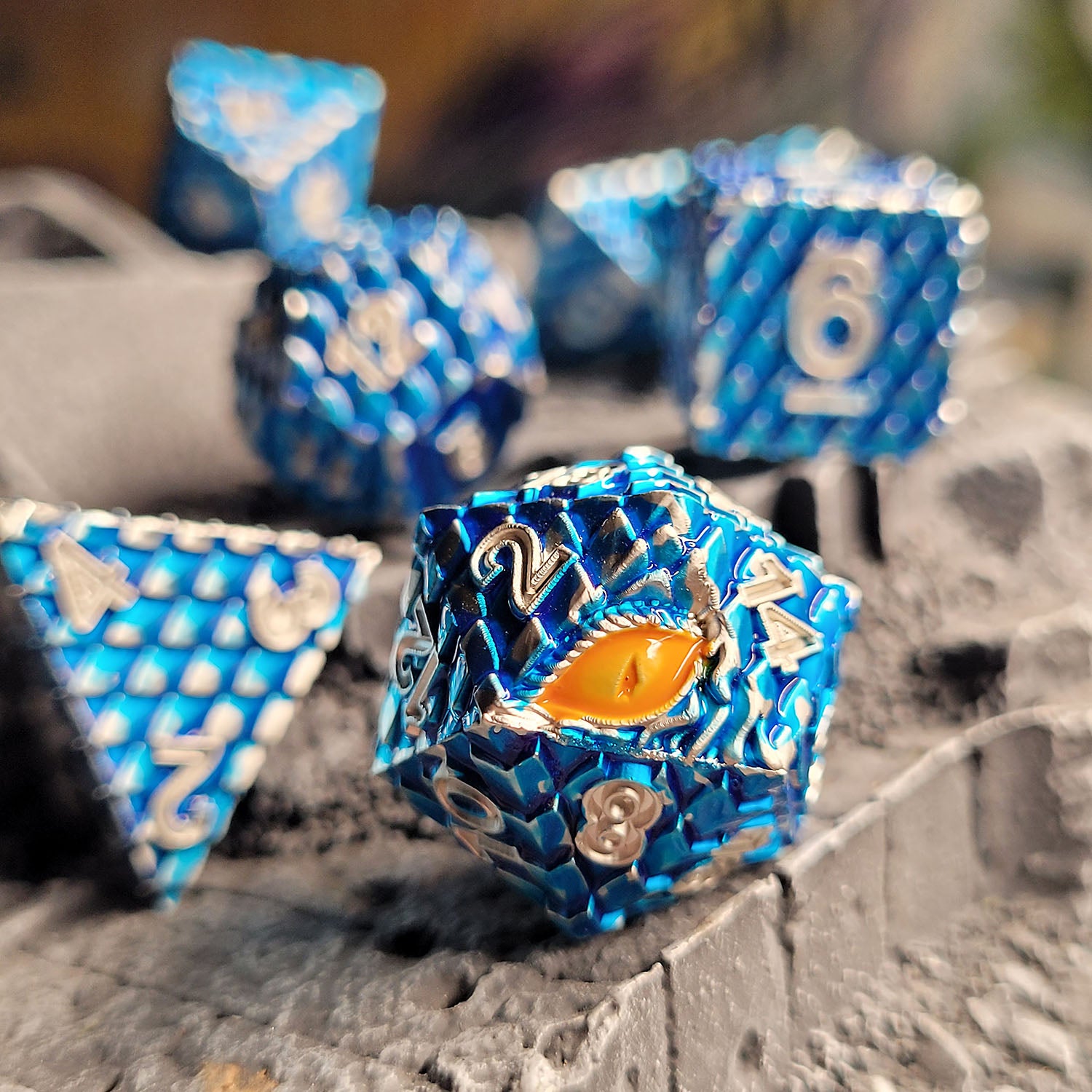 This is an environmental image of the Forged Gaming Dragon's Gaze Blue Metal RPG Dice Set. The photo was taken using a piece of stone wargaming terrain as a background.