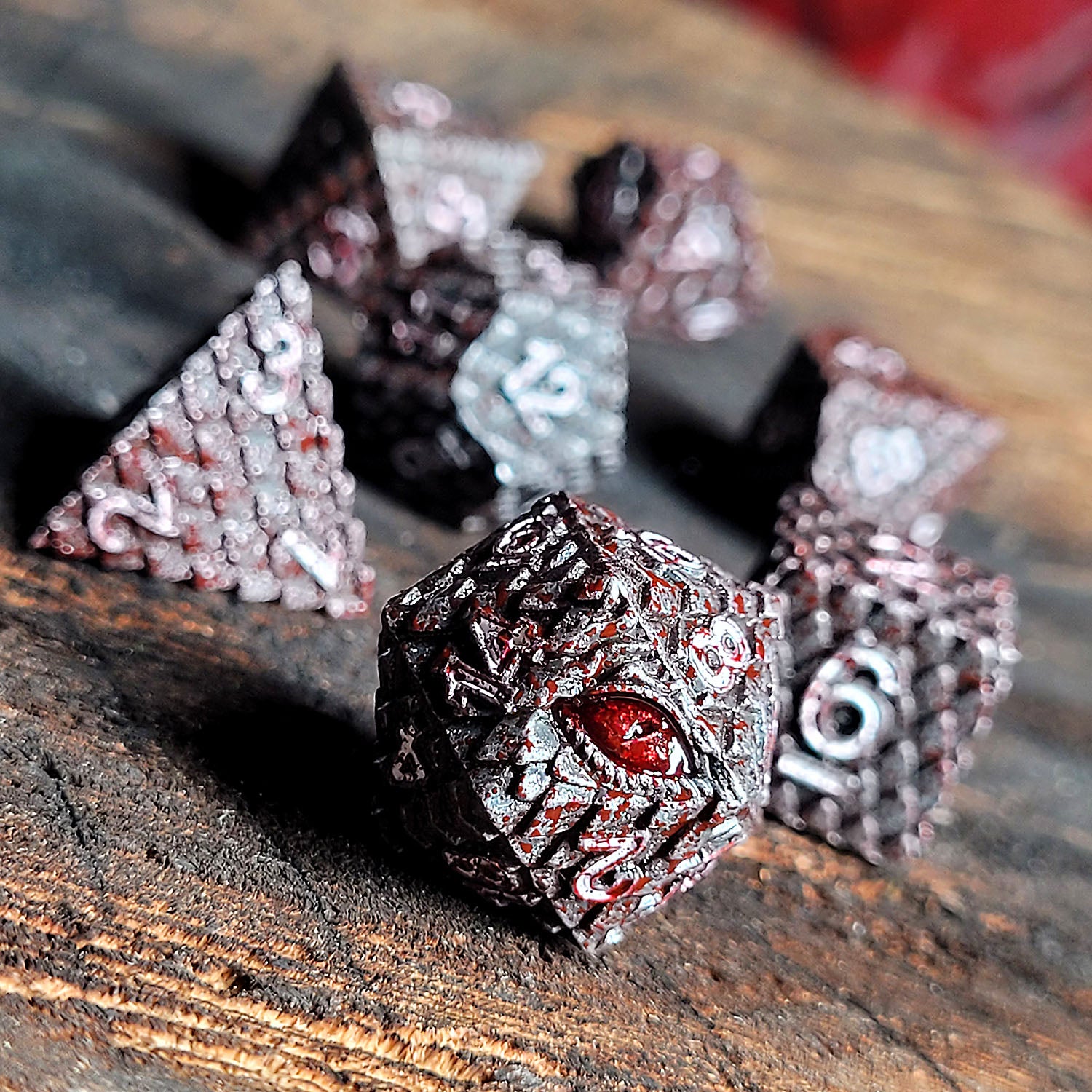 Environmental photo of Forged Gaming Dragon's Gaze Silver Blood Metal RPG Dice Set sitting on a burned wood platform.