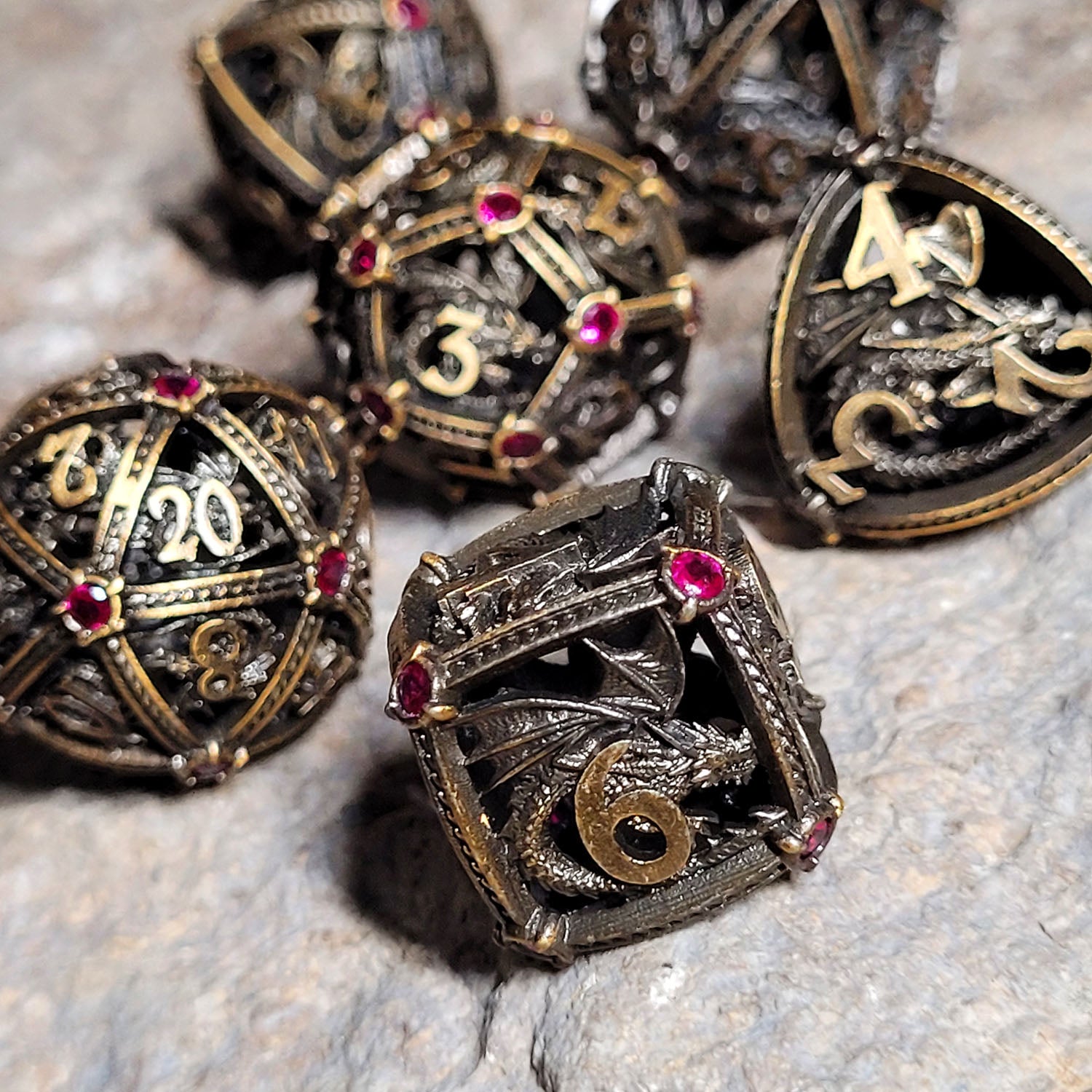 This is an environmental image of the Dragon's Jewel Bronze Hollow Metal RPG Dice Set. The photo was taken using a piece of stone wargaming terrain as a background.