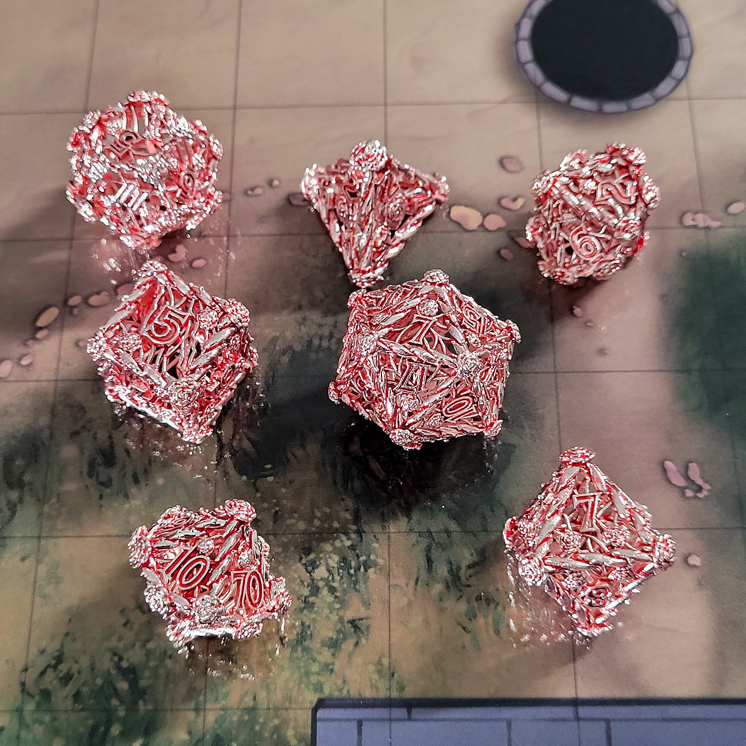 This is an environmental image of the Forged Gaming Enchanted Rose Silver Red Hollow Metal RPG Dice Set. The photo was taken against the background of the City Streets Encounter Map.