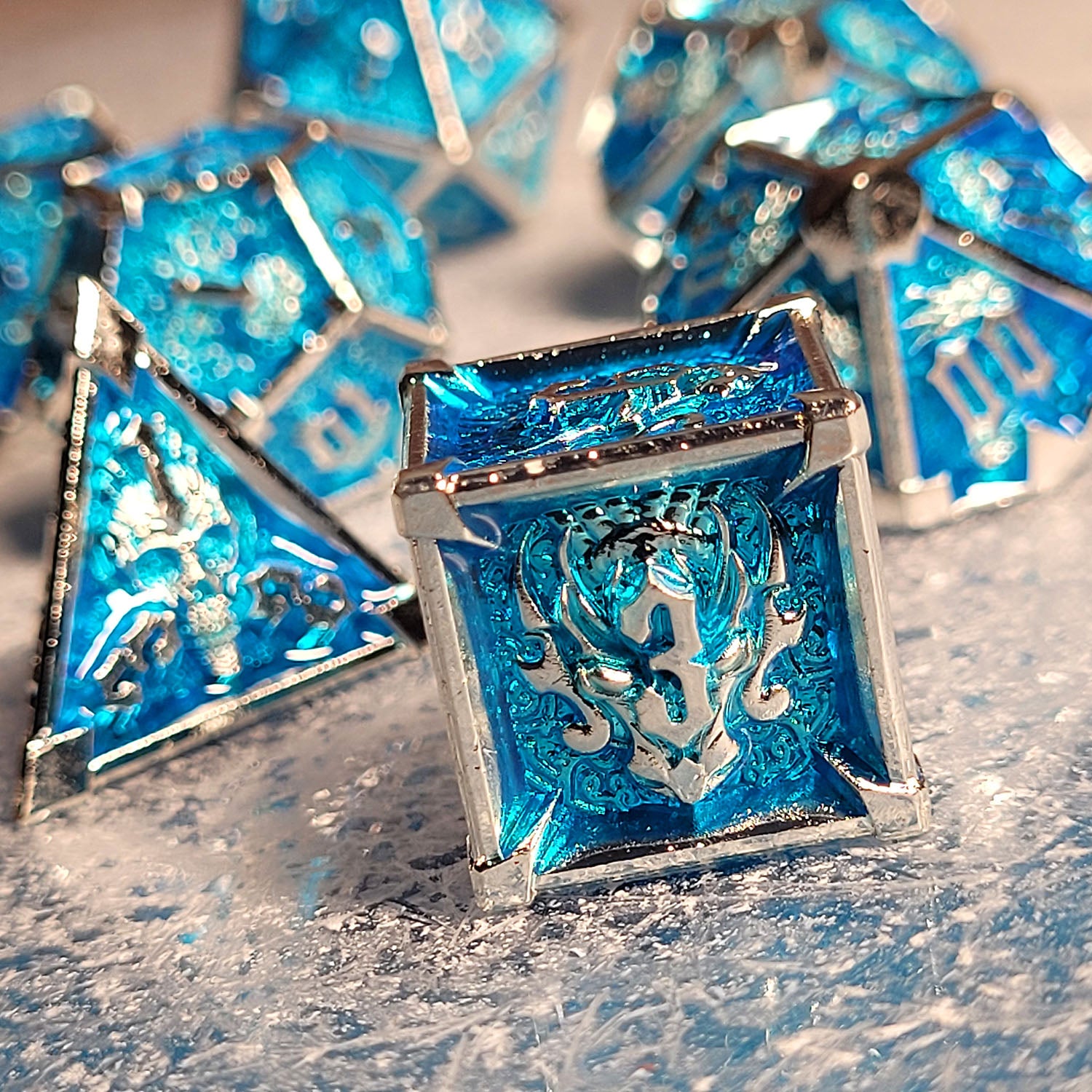 This is an environmental image of the Forged Gaming Ossuary Obscura Silver Blue Metal RPG Dice Set. The image was taken using a snowflake-pattern substrate as a background.