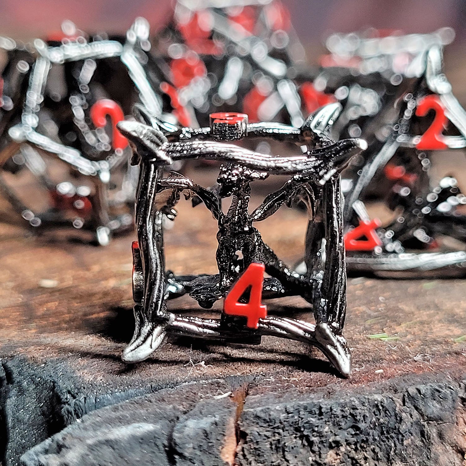 This is an environmental image of the Forged Gaming Wicker Dragon Silver Hollow Metal RPG Dice Set. The photo was taken using a piece of scorched wood as a background.