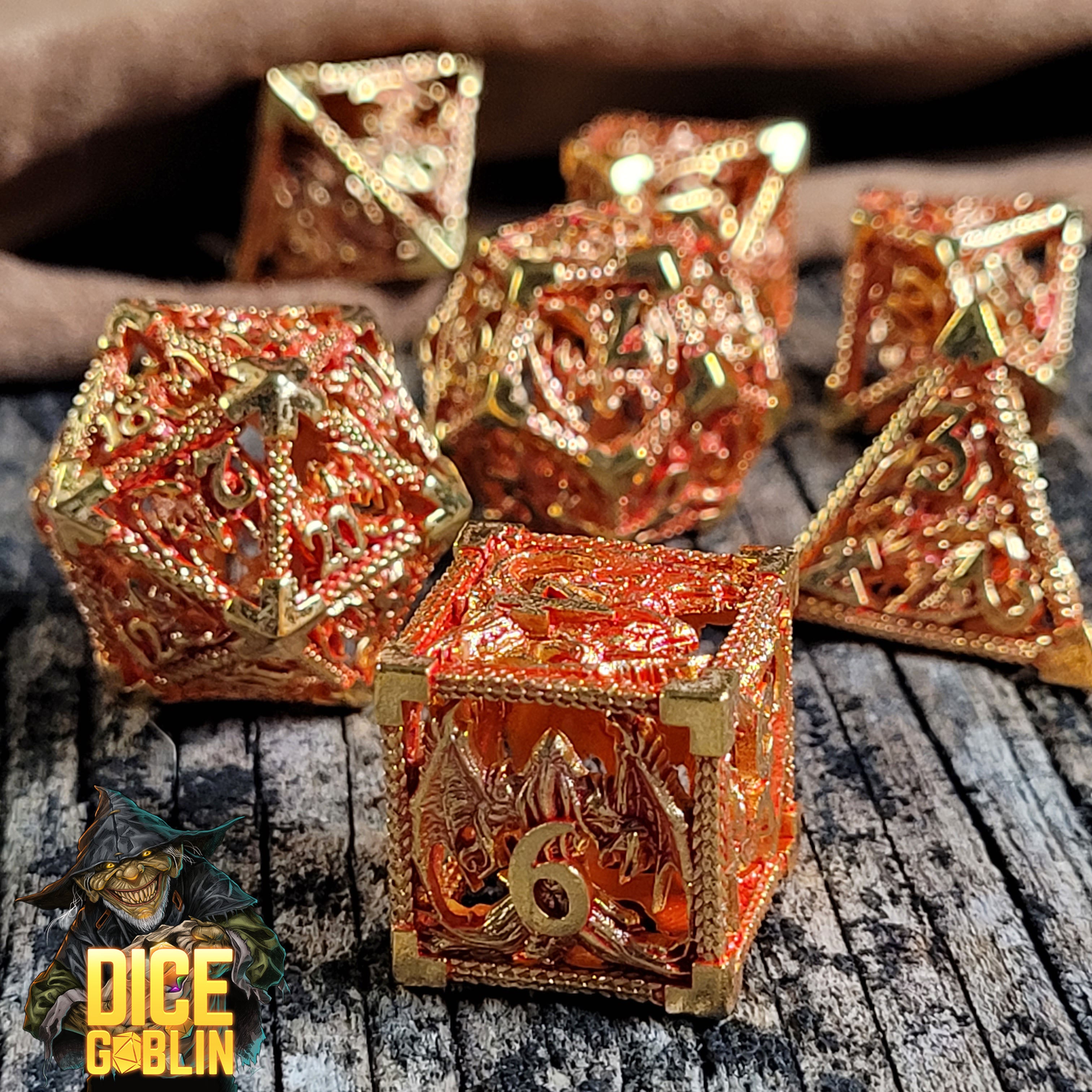 This is an environmental image of the Dice Goblin Dragon Rampant Gold Red Hollow Metal RPG Dice Set taken on a distressed wood surface.