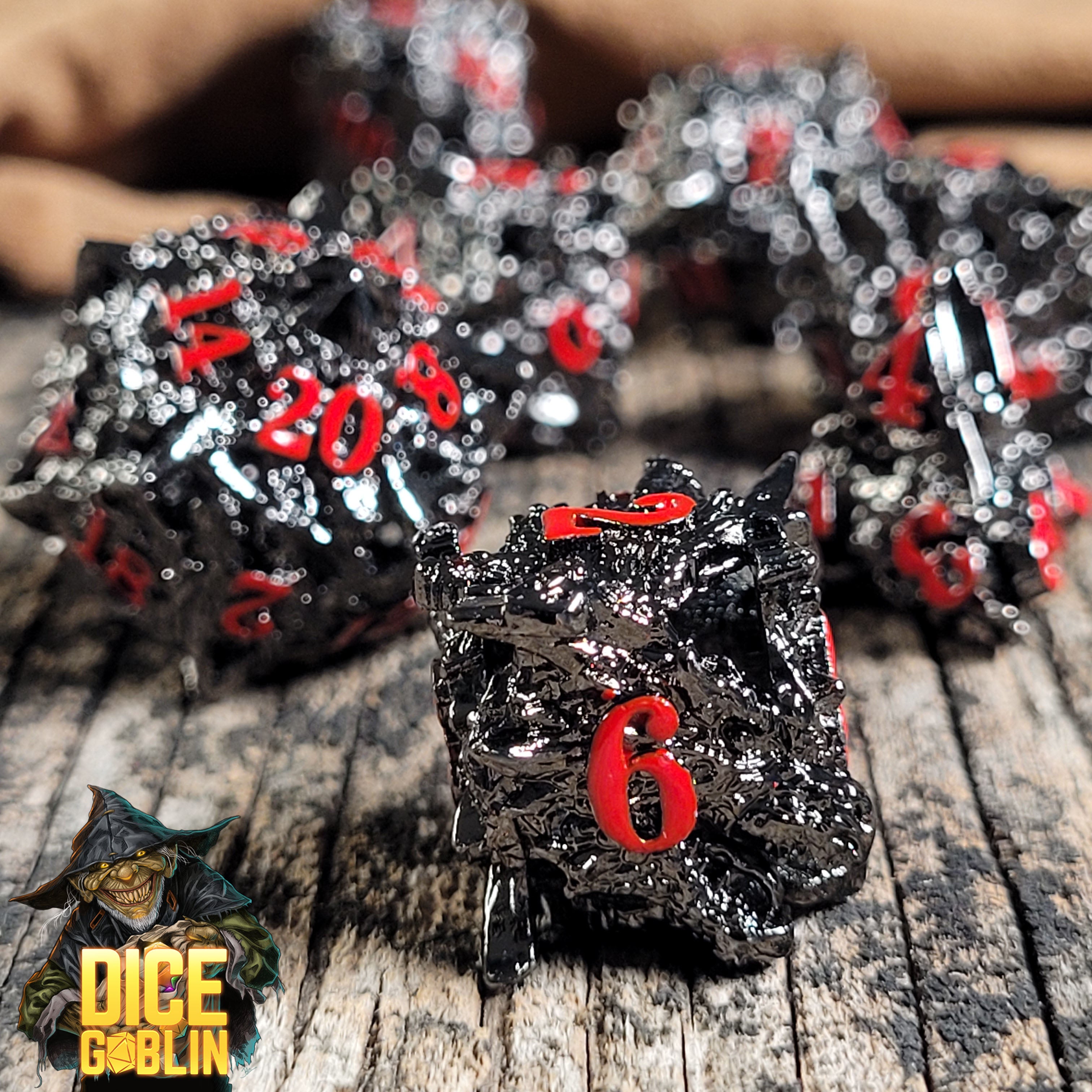 This is an environmental image of the Dice Goblin Dragon's Head Black with Red Hollow Metal RPG Dice set on a distressed wood surface.