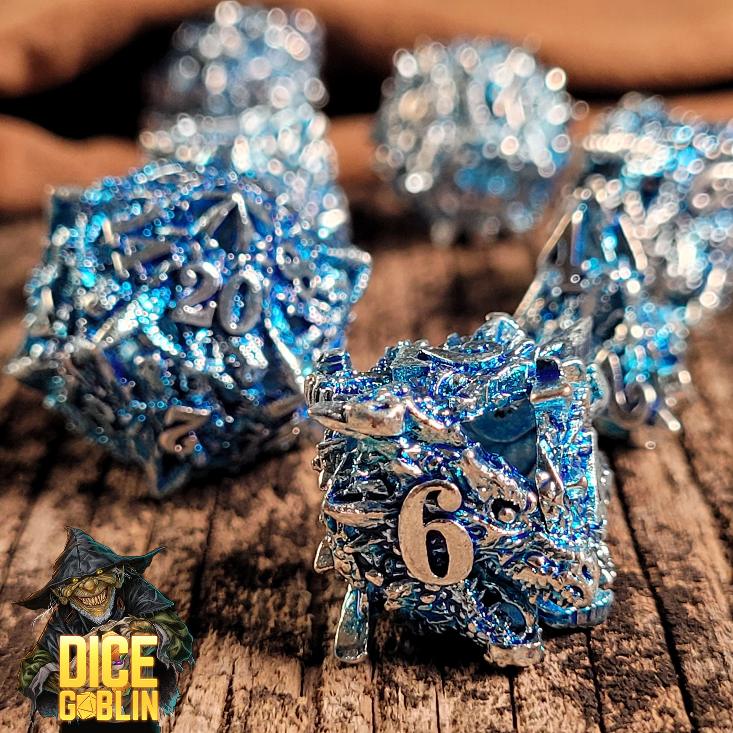 This is an environmental image of the Dice Goblin Dragon's Head Silver with Blue Wash Hollow Metal RPG Dice set on a distressed wood surface.