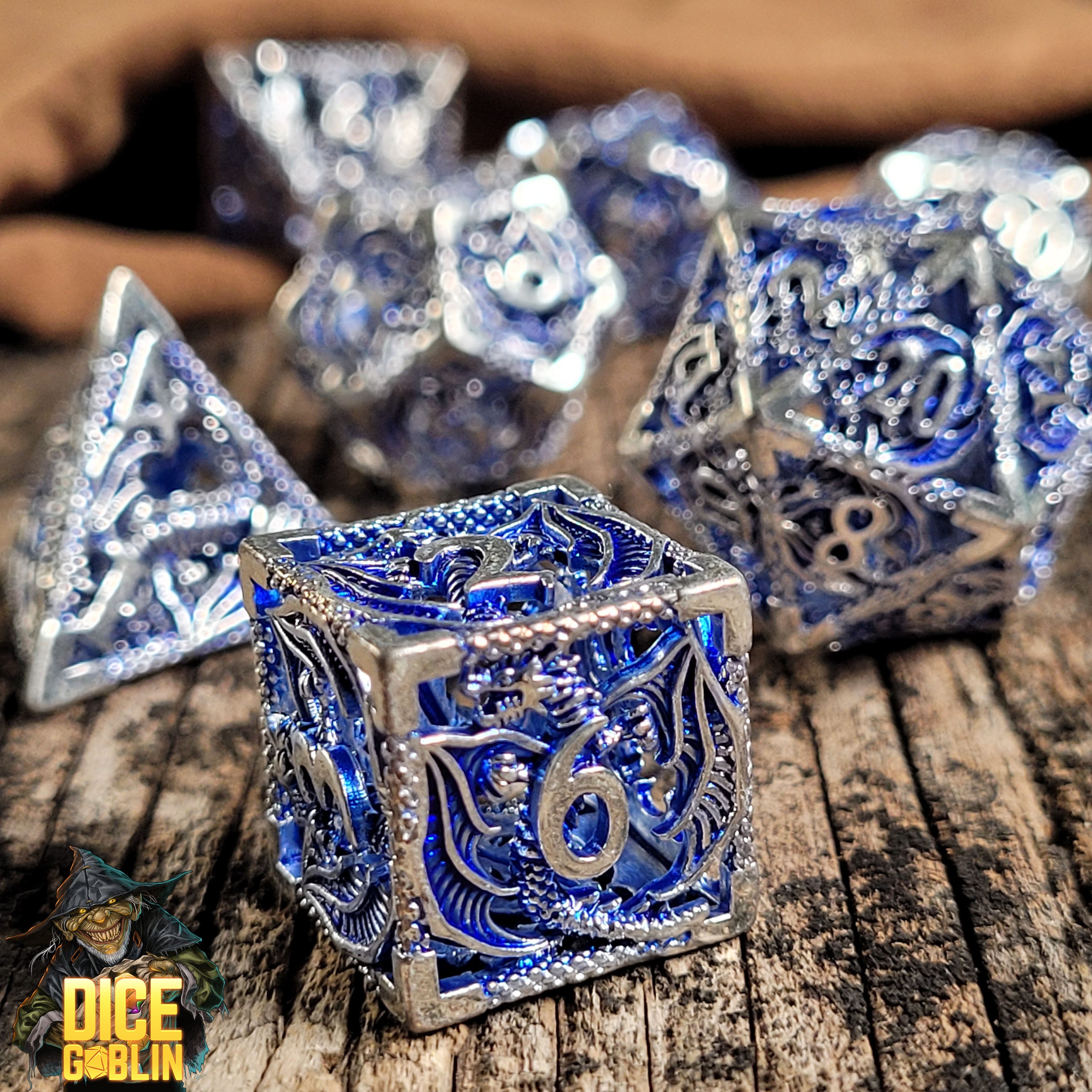 This is an environmental image of the Dice Goblin Dragon Rampant Silver with Dark Blue Wash Hollow Metal RPG Dice Set taken on a distressed wood surface.