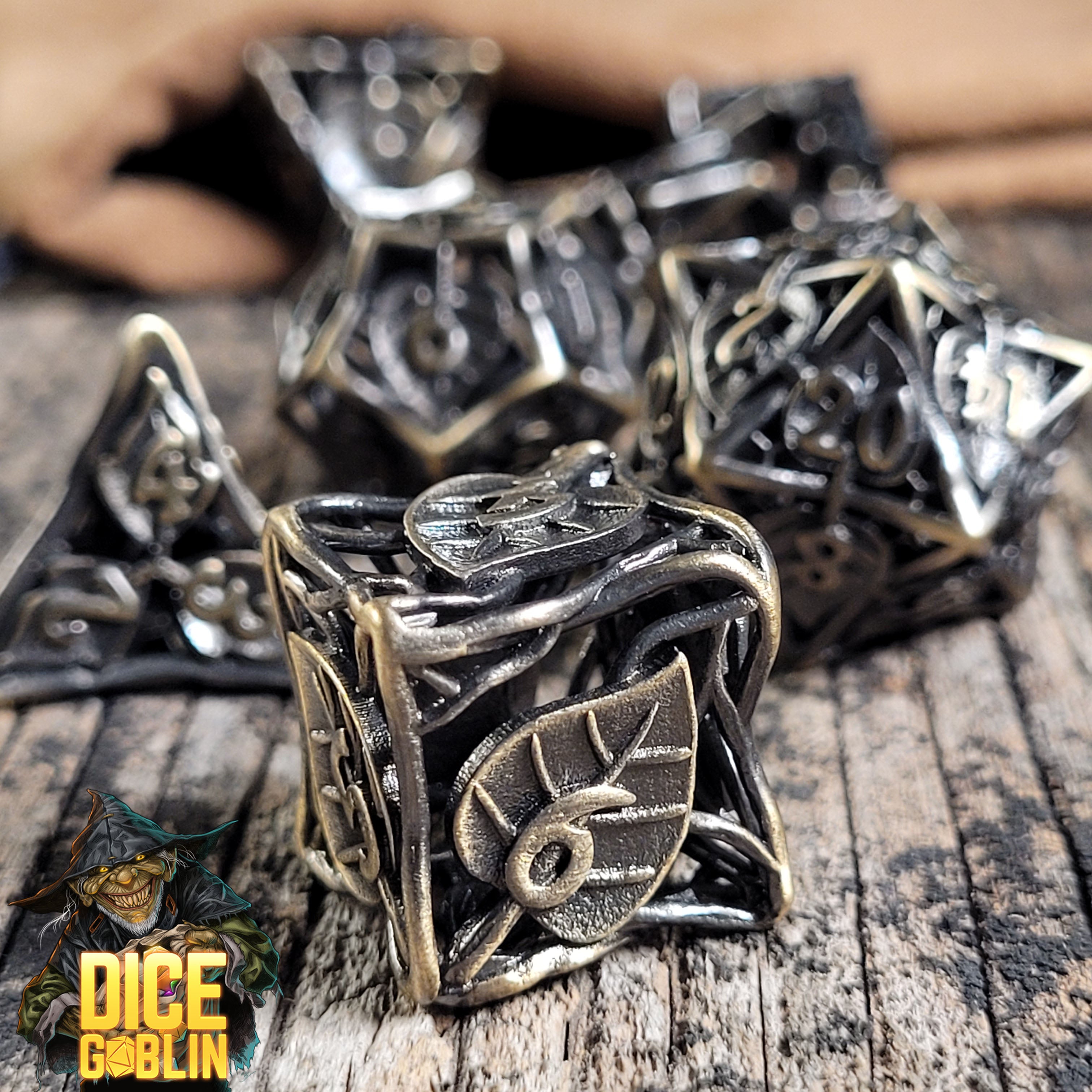 This is an Environmental image of the Dice Goblin Leaves Weathered Gold Hollow Metal RPG Dice Set on a distressed wood surface.
