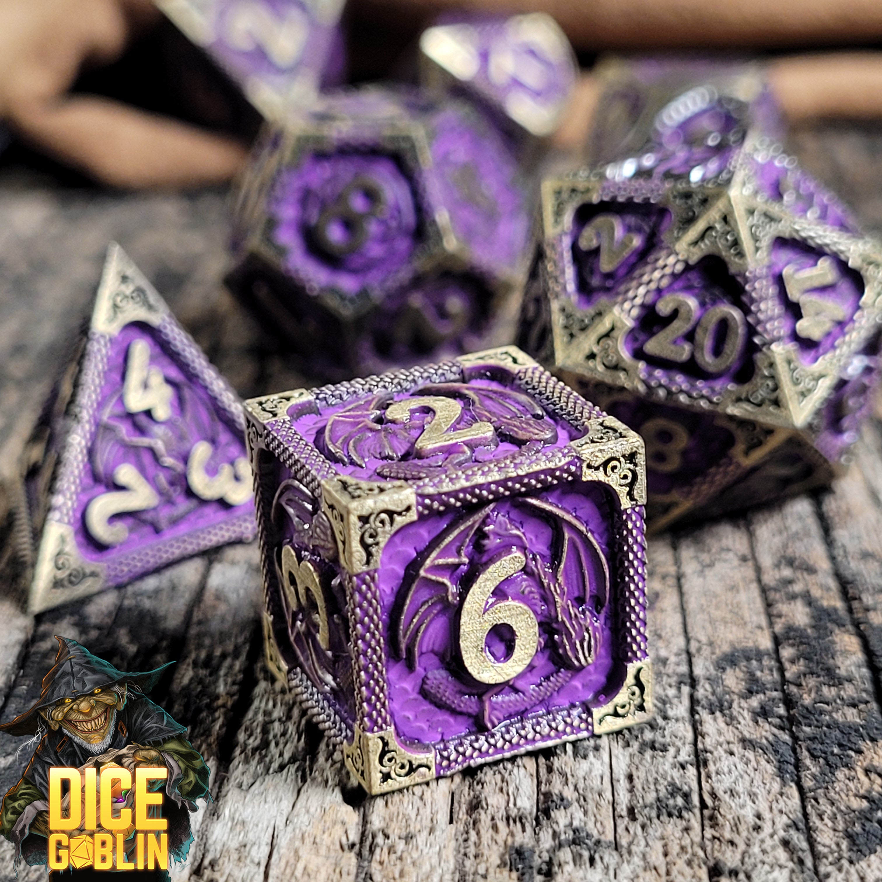This is an environmental image of the Dice Goblin Dragon's Breath Weathered Gold and Purple Metal RPG Dice Set on a distressed wood surface