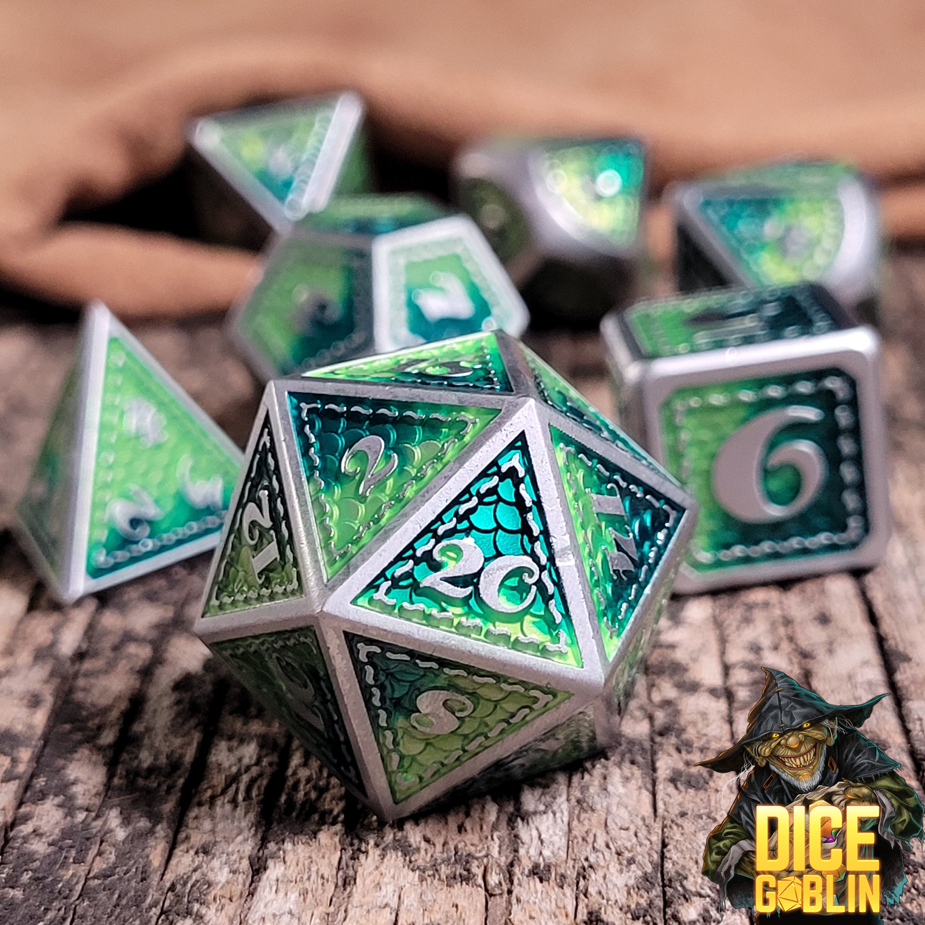 This is an environmental image of the Dice Goblin Silver and Two-Tone Metallic Green Metal RPG Dice Set on a distressed wood surface.