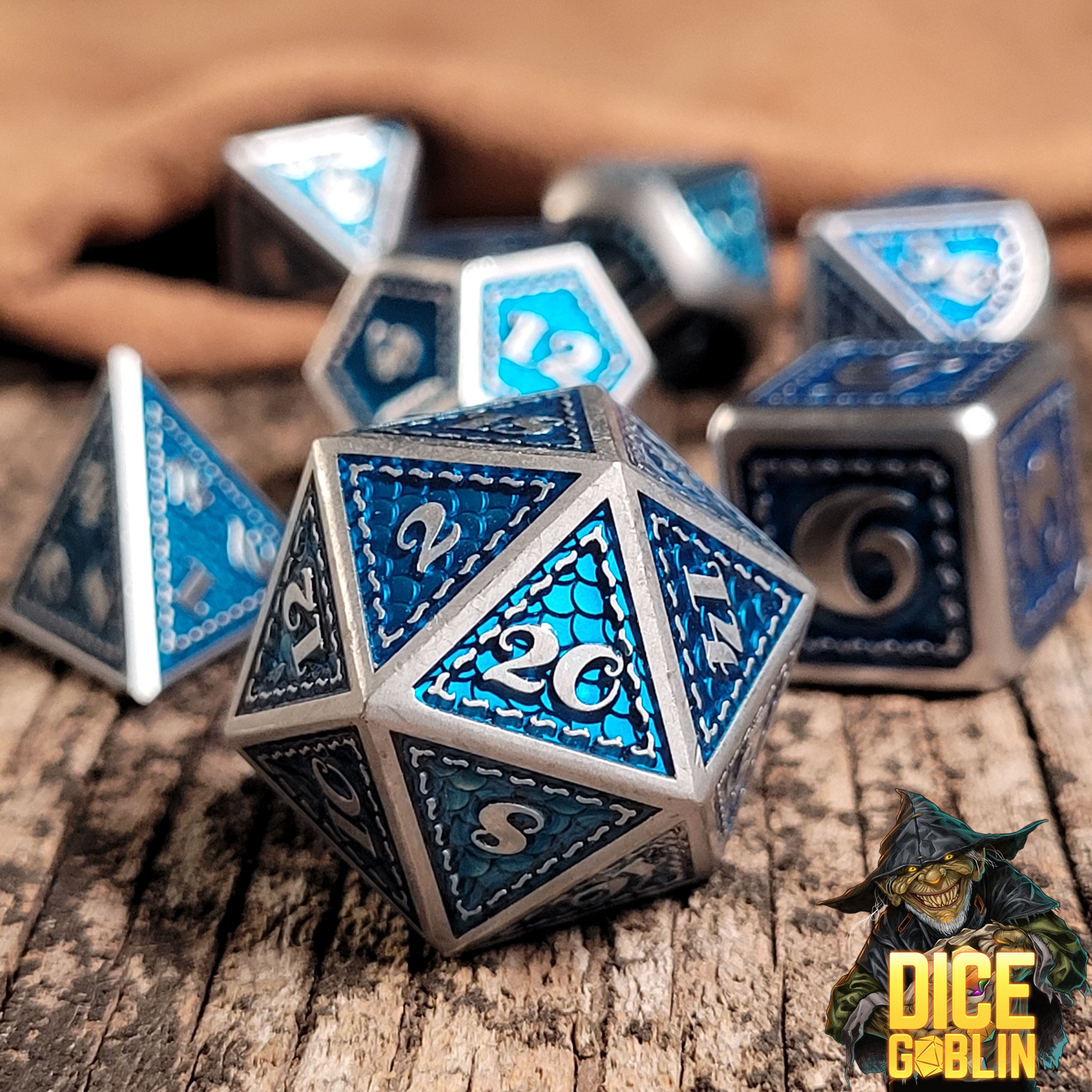 This is an environmental image of the Dice Goblin Silver and Metallic Blue Metal RPG Dice Set on a distressed wood surface.