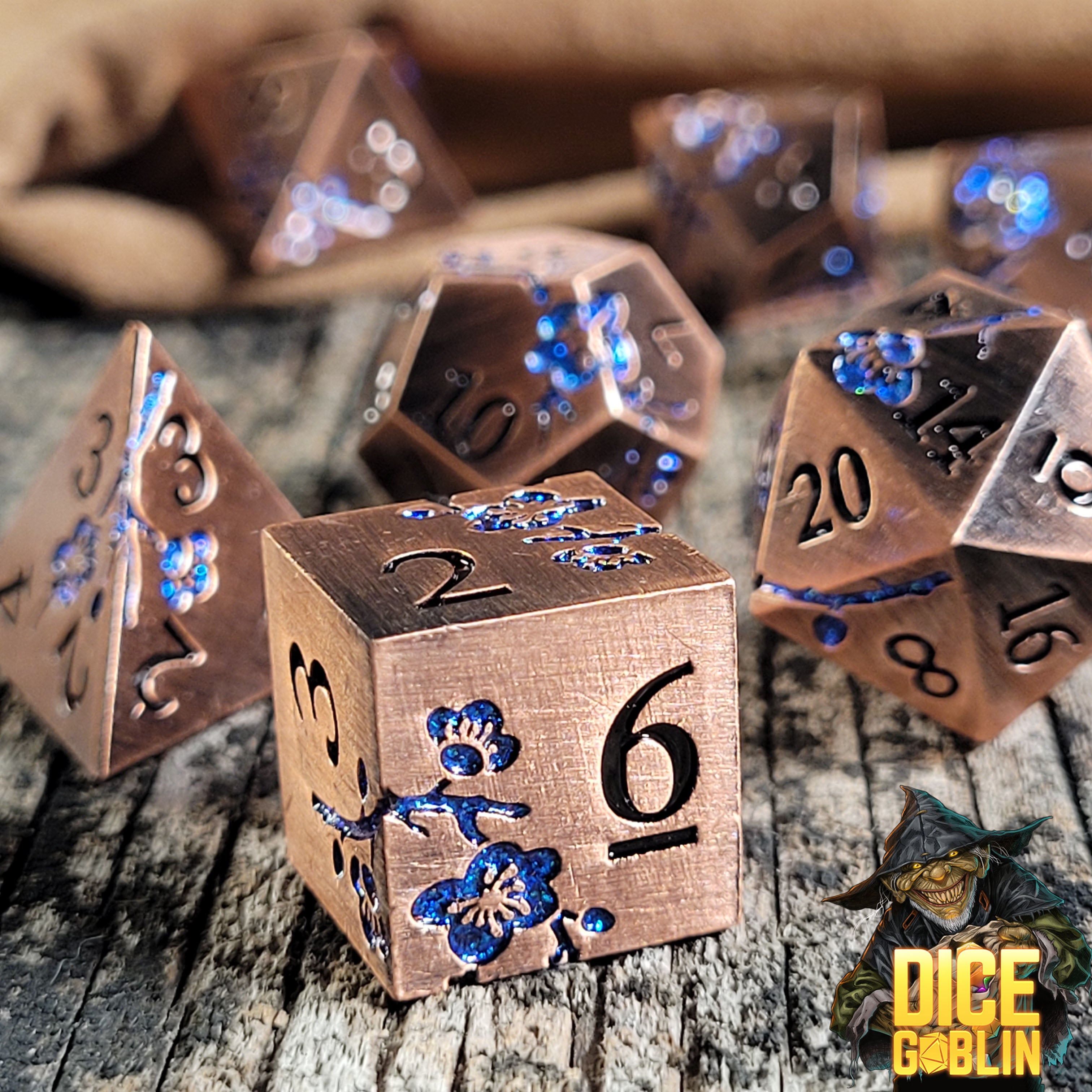 This is an environmental image of the Dice Goblin Flowers Copper with Blue Glitter Metal RPG Dice Set on a distressed wood surface.