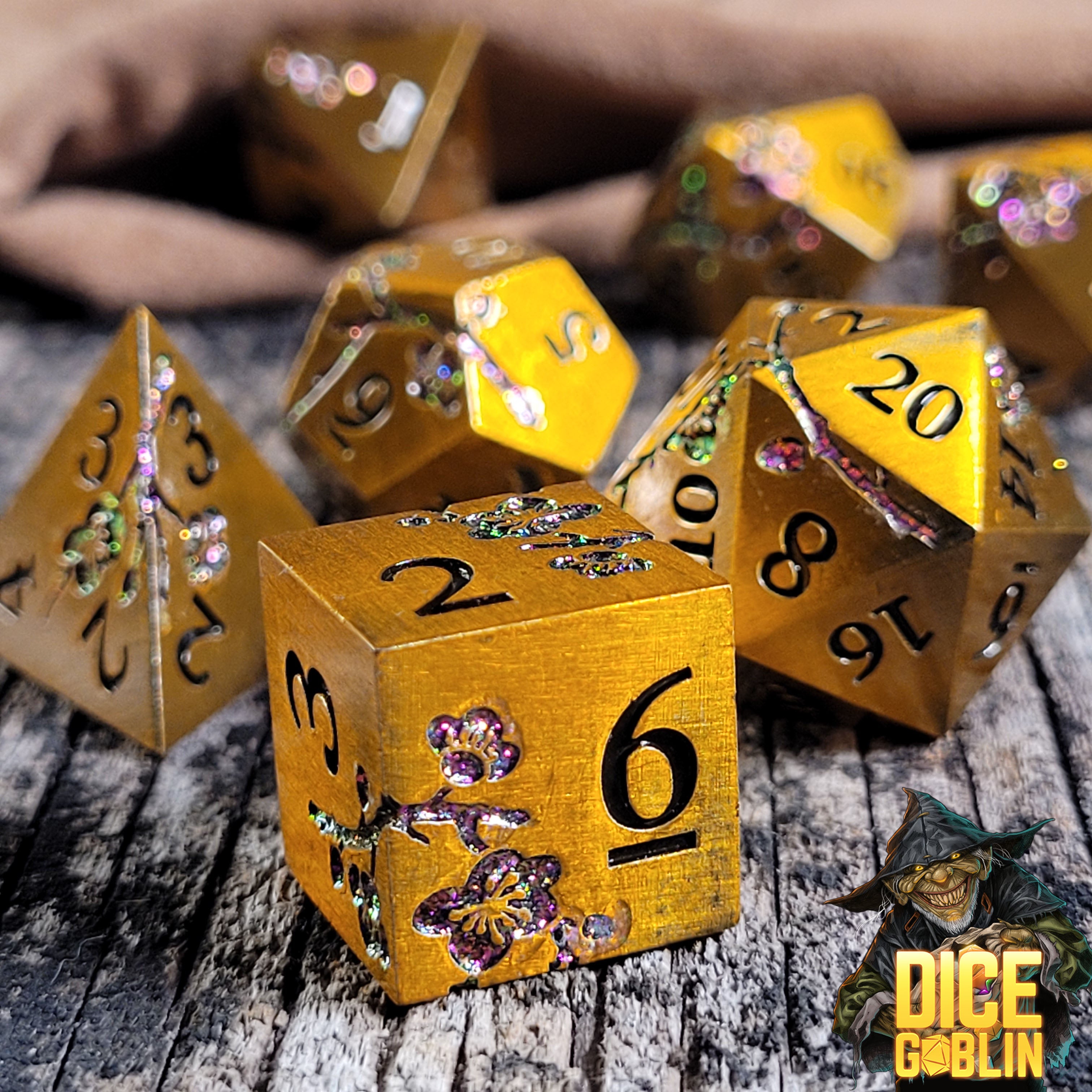 This is an environmental image of the Dice Goblin Flowers Gold with Purple Glitter Metal RPG Dice Set on a distressed wood surface.