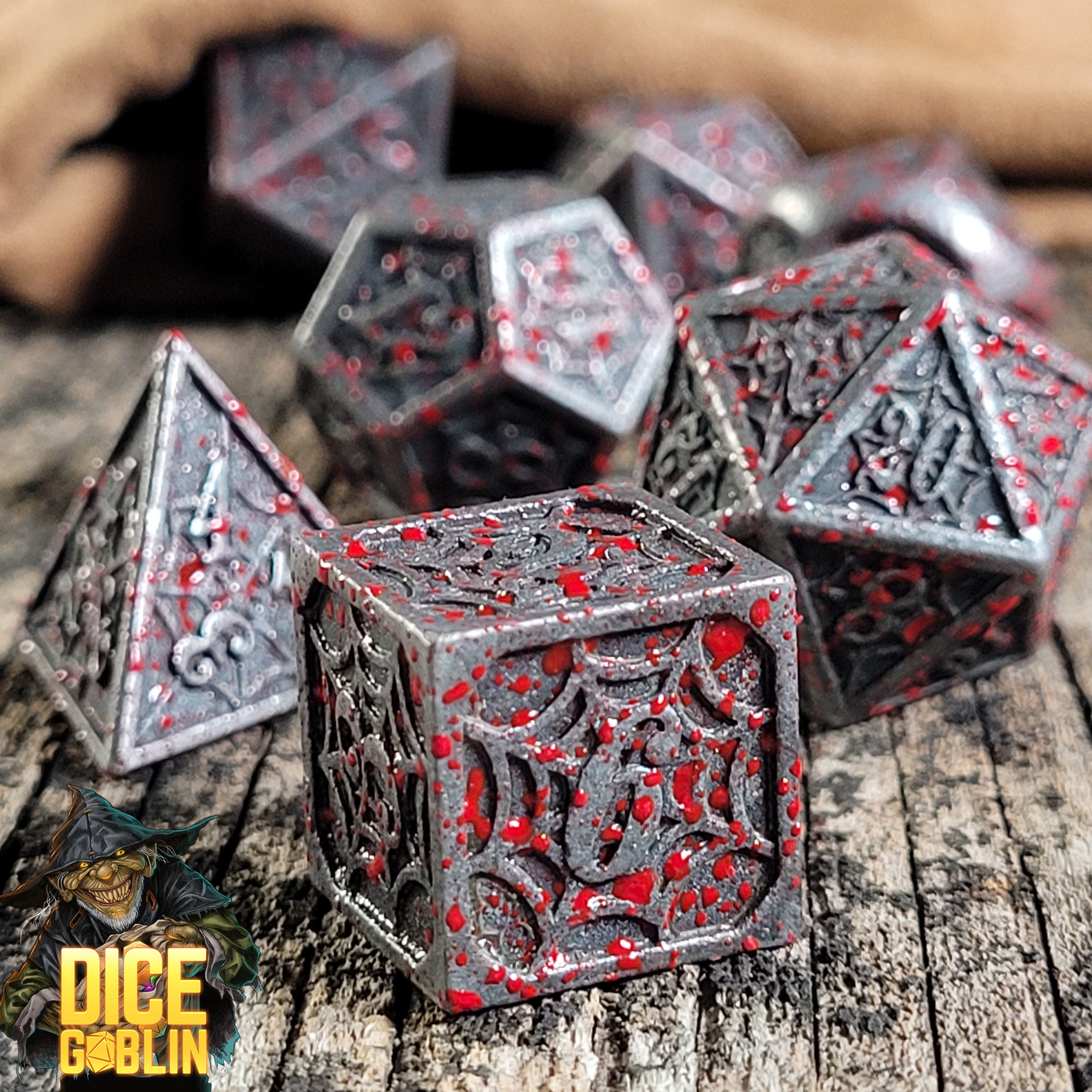 This is an environmental image of the Dice Goblin Webs Weathered Silver with Blood Splatter Metal RPG Dice set on a distressed wood surface.