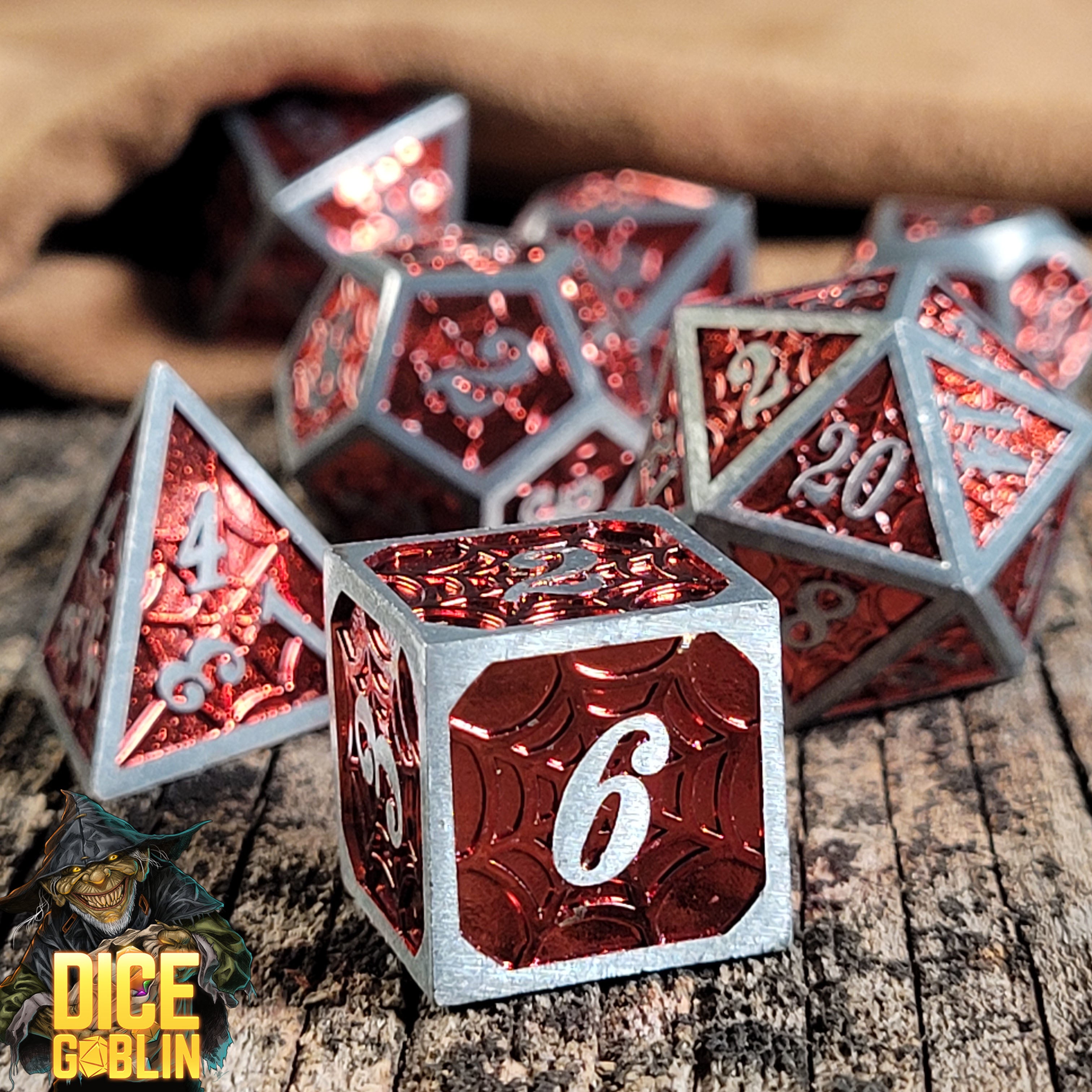 This is an environmental image of the Dice Goblin Webs Silver and Metallic Red Metal RPG Dice set on a distressed wood surface.