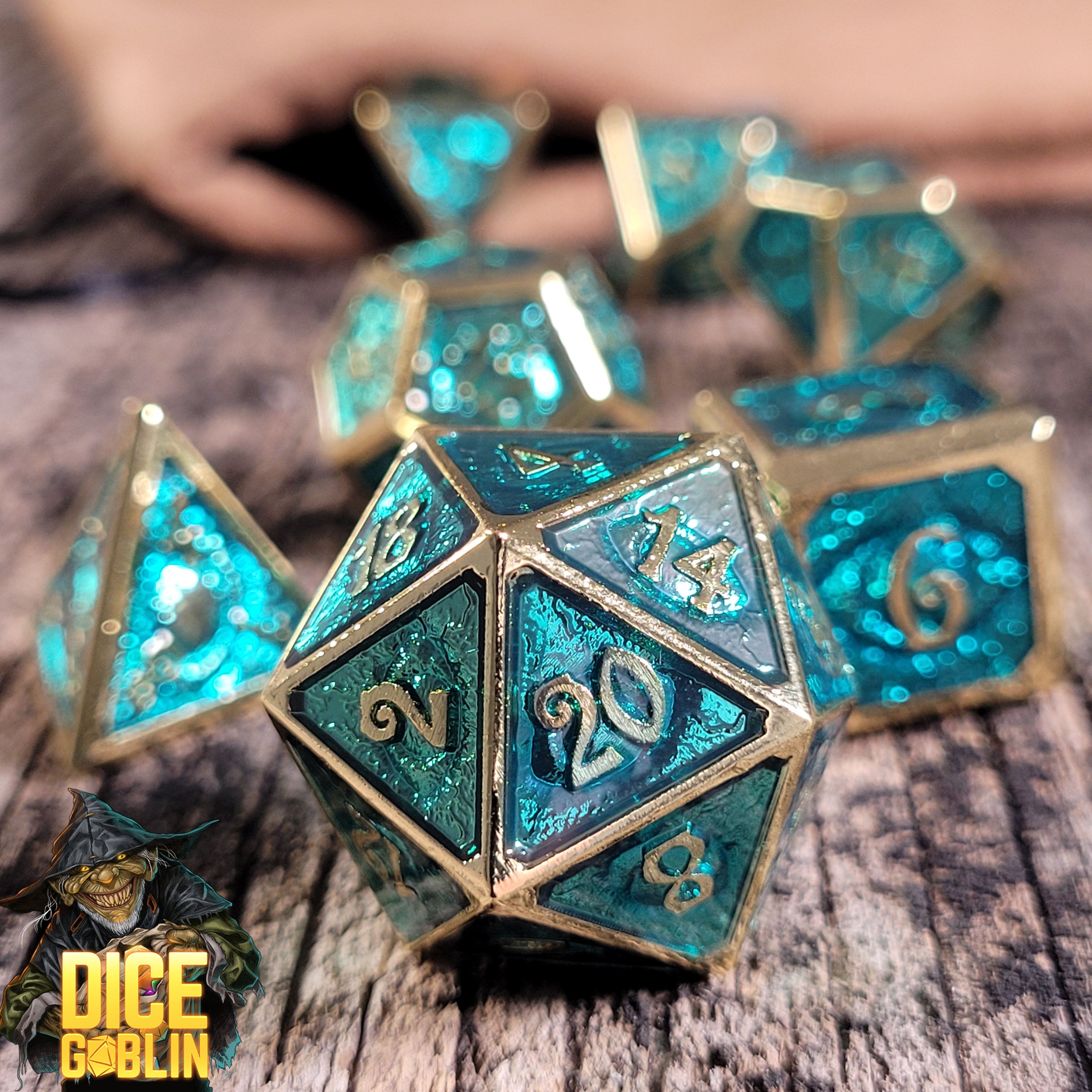 This is an environmental image of the Dice Goblin Eyes Gold with Foiled Teal Metal RPG Dice Set on a distressed wood surface.