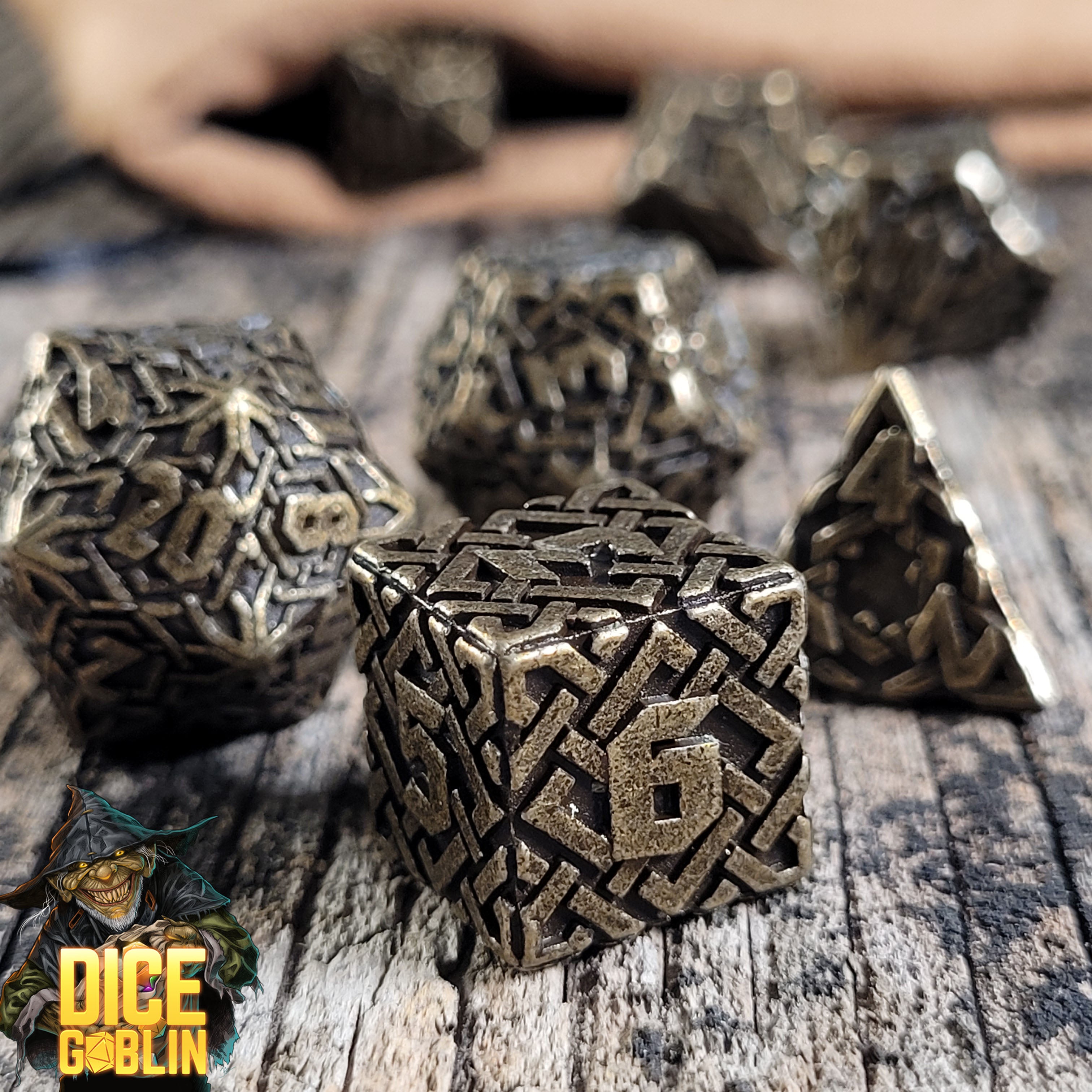 This is an environmental image of the Dice Goblin Knots Weathered Bronze Metal RPG Dice Set on a distressed wood surface.