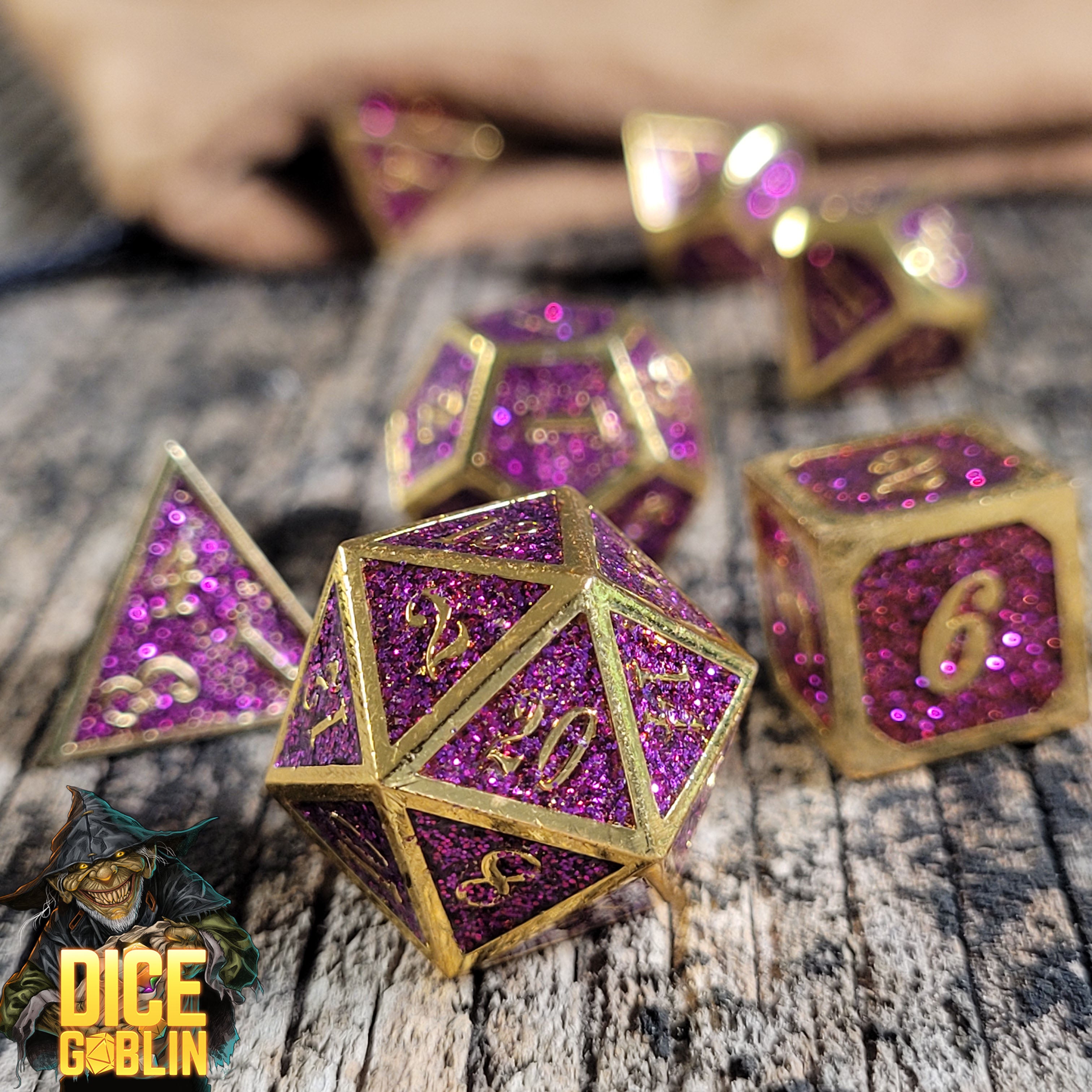 This is an environmental image of the Dice Goblin Framed Gold with Purple Glitter Metal RPG Dice Set on a distressed wood surface.