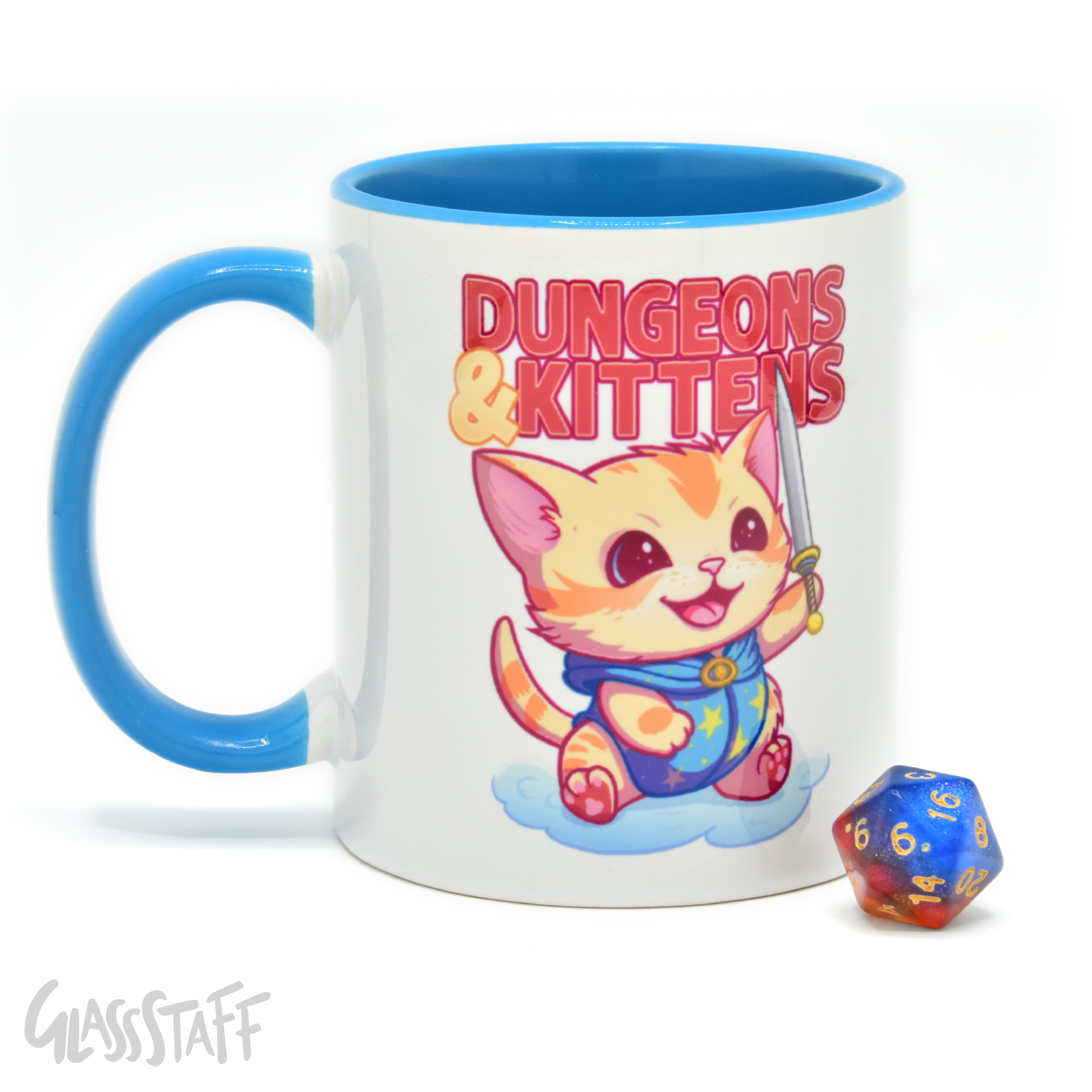 This is a white background image of the GLassStaff Dungeons and Kittens ceramic mug. It shows the white mug with a blue handle, blue inside, and Dungeons and Kittens design. It also shows the D20 die included with the mug.