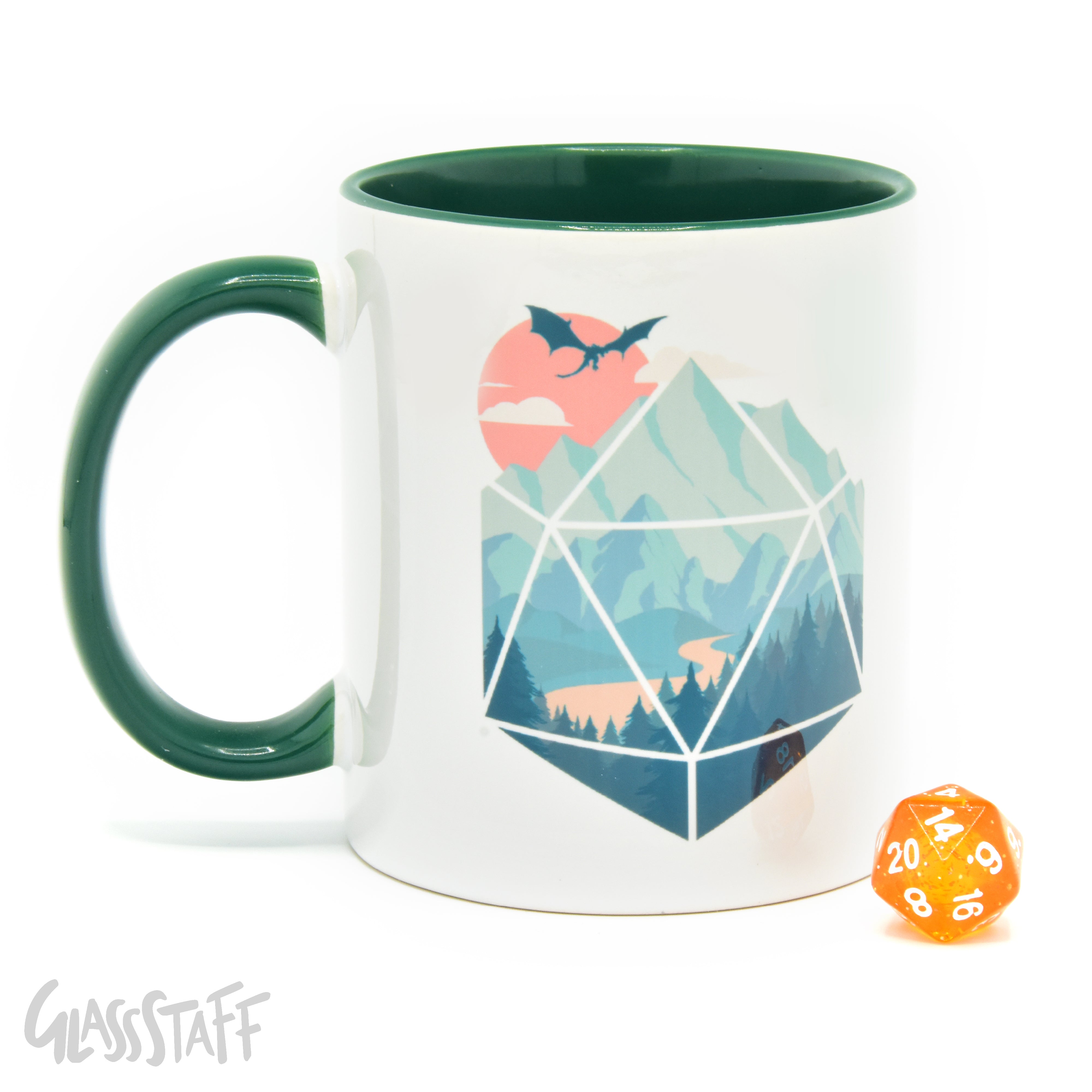 This is a white background image of the GLassStaff D20 Scene ceramic mug. It shows the white mug with a green handle, green inside, and D20 scene design. It also shows the D20 die included with the mug.